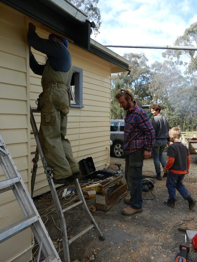 Volunteers on a ladder repairing the school verandah during a community working bee